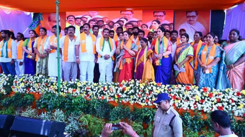 Leaders in saffron scarves on a flower-decked stage with large portraits behind them