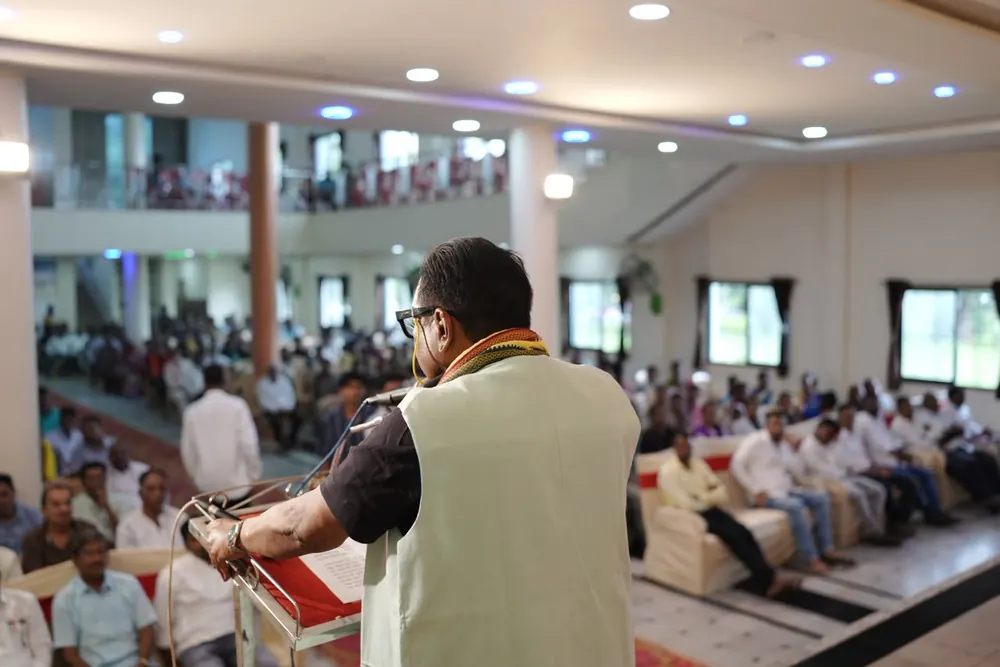 A speaker addressing a seated audience in a hall, seen from behind