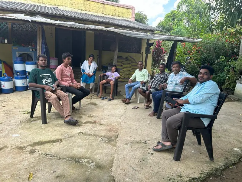 Team members sitting in a circle on chairs in a village courtyard