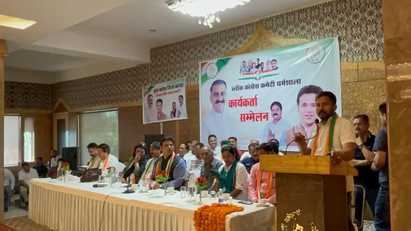 A speaker at a podium addressing a gathering in a hall, with leaders seated at a table