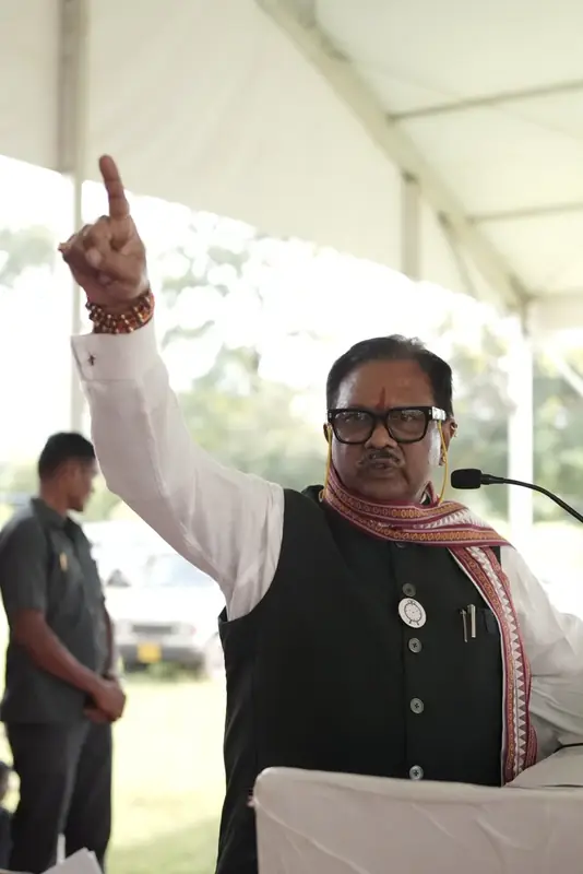 A speaker pointing upward while addressing a gathering under a tent